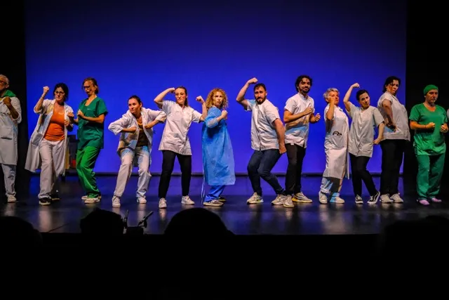 Les interprètes du spectacle « 99 soignant.e.s », en blouse et en tenue de bloc, alignés sur scène le poing levé.