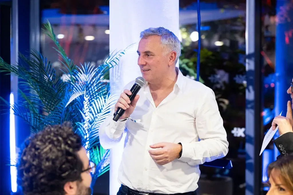 Un intervenant en chemise blanche prend la parole devant les invités.