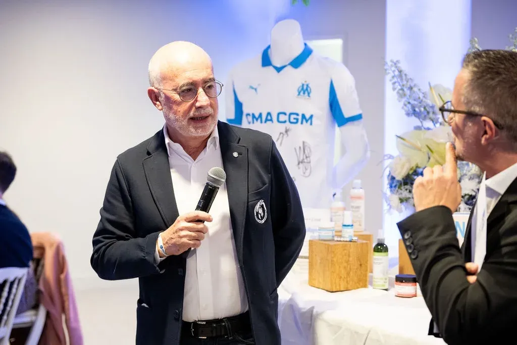 Un intervenant au micro devant le maillot CMA CGM de l’Olympique de Marseille dédicacé par les joueurs.