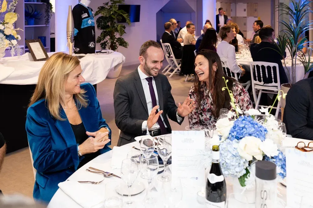 Trois convives rient ensemble à table, devant la flamme olympique mise en jeu.