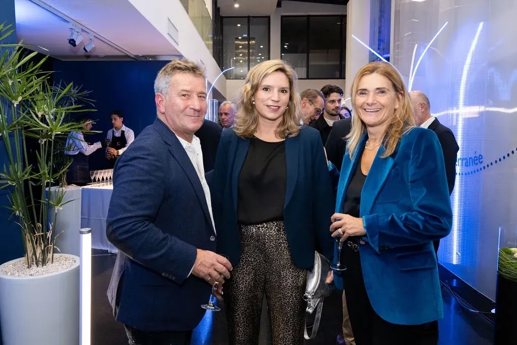 Trois invités posent ensemble à l’accueil de la soirée, coupe à la main.