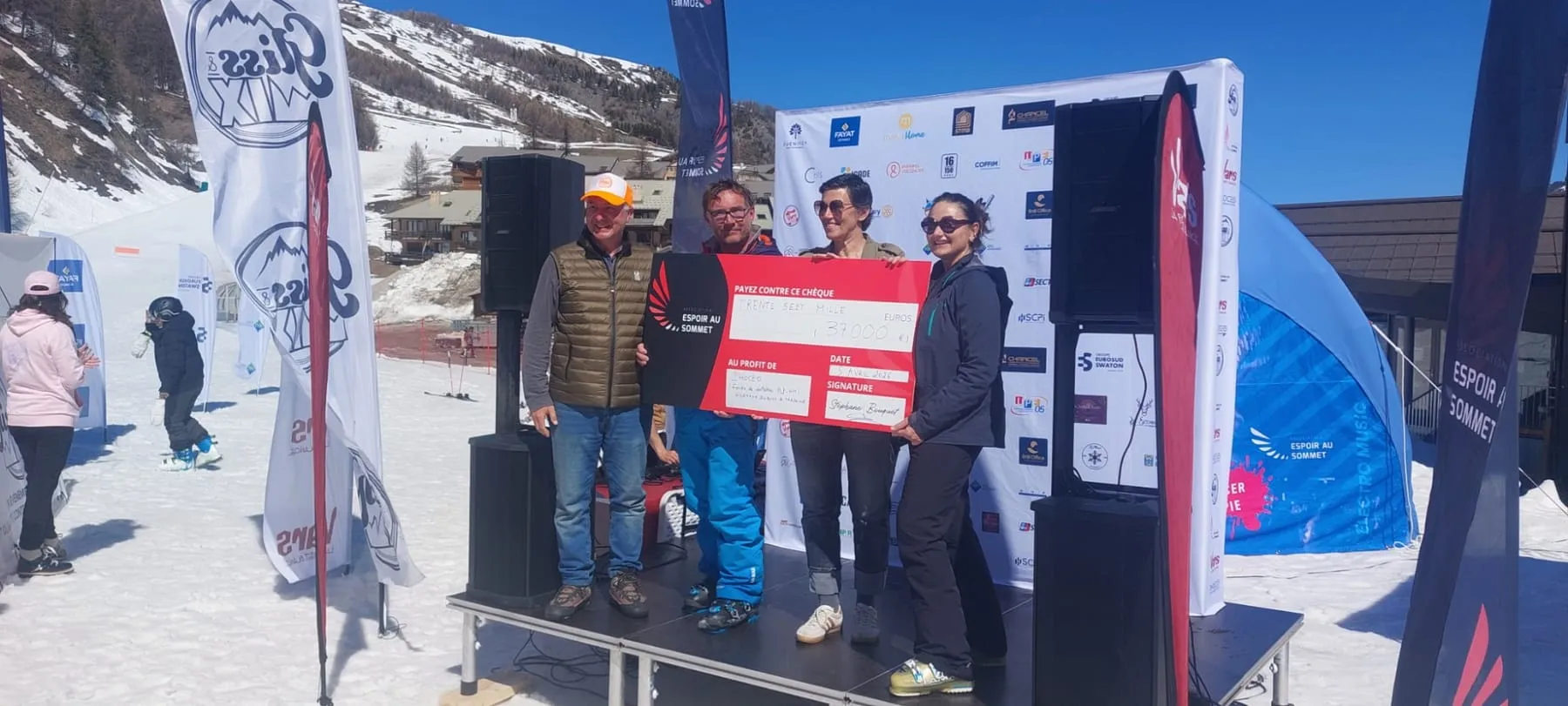 Sur la scène de Vars, quatre personnes présentent le chèque de 37 000 € d’Espoir au sommet au profit de Phoceo, fonds de dotation de l’AP-HM.