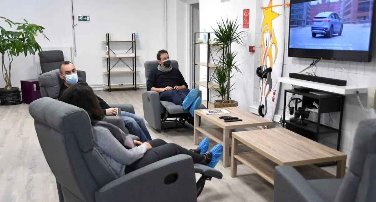 Un espace de repos aménagé pour les patients : fauteuils inclinables, écran et plantes.