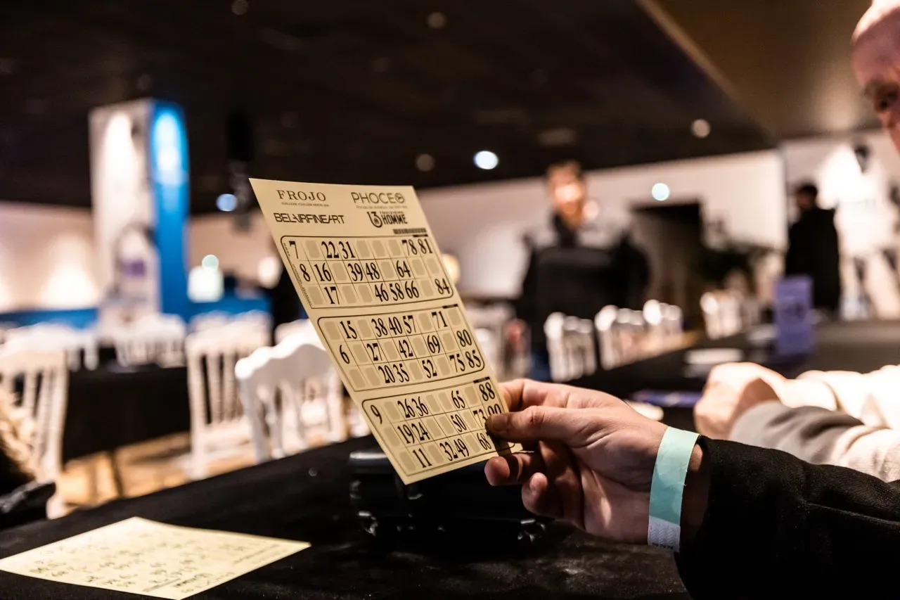 Un participant tient son carton de loto, aux logos de Phoceo et des partenaires de la soirée.