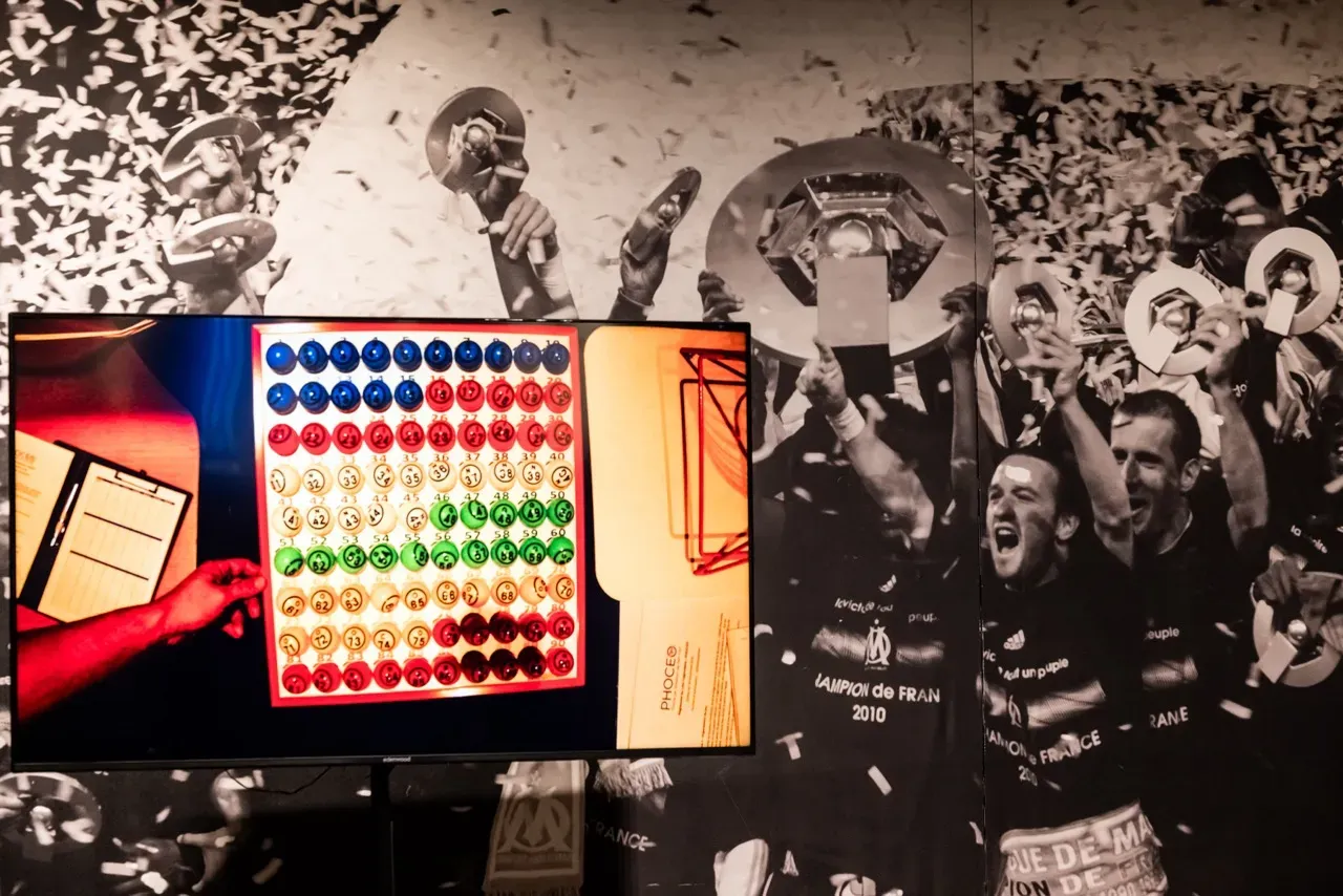 L’écran de jeu affiche le plateau des numéros, devant une fresque des joueurs de l’OM champions de France.