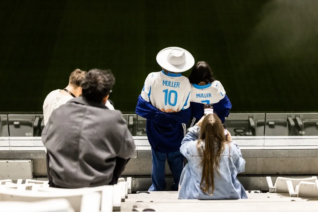 Deux invités photographiés de dos face à la pelouse, en maillot floqué « Muller ».