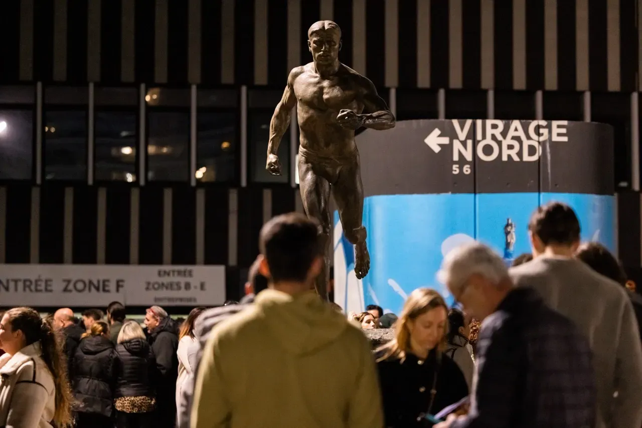 La statue du coureur devant l’entrée du virage Nord, au milieu des invités qui arrivent.