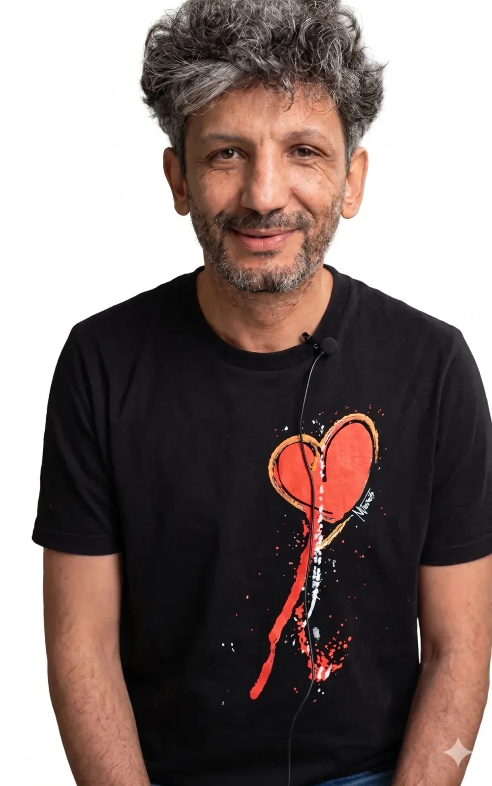 Portrait souriant d’un homme en tee-shirt orné d’un cœur peint, micro-cravate au col.
