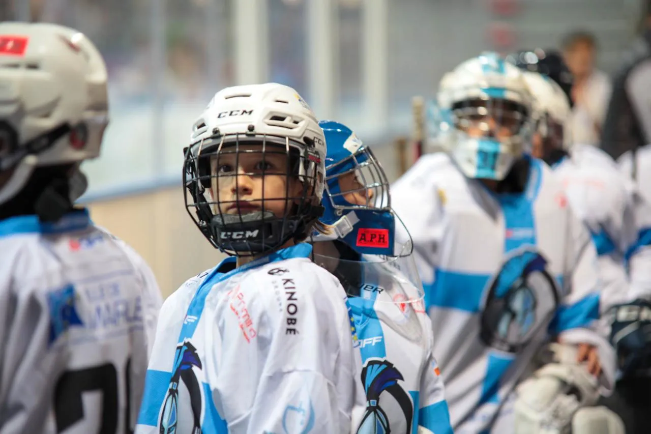 De jeunes joueurs du hockey mineur des Spartiates de Marseille, casque et maillot du club, au bord de la patinoire.